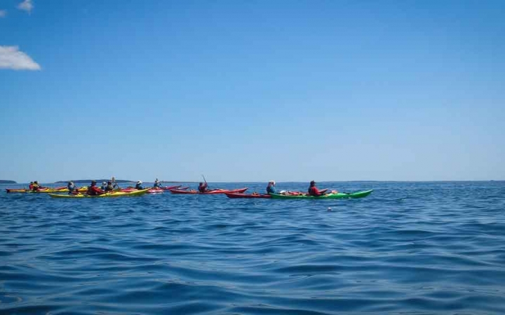 a group of people paddle kayaks on blue open water under blue skies